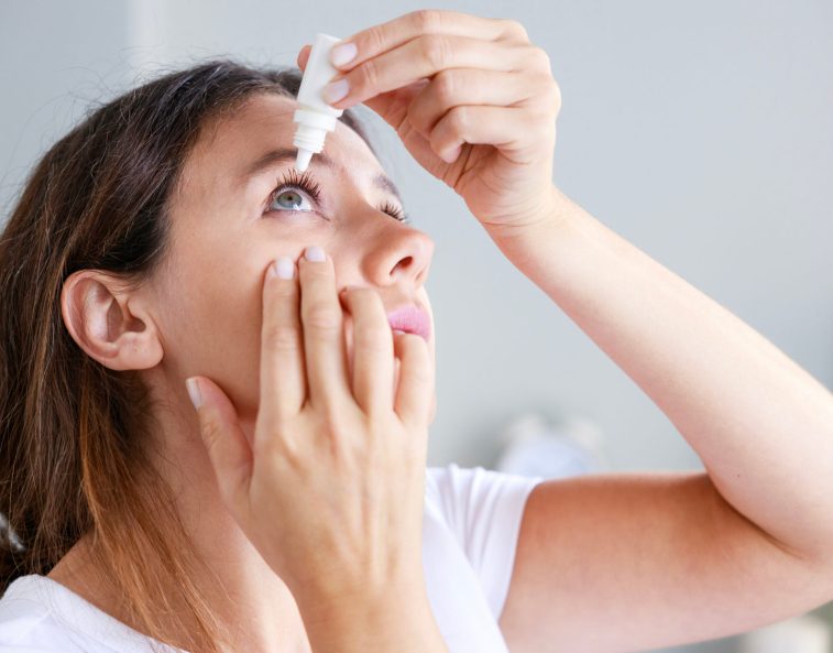 Young woman putting eye drops at home